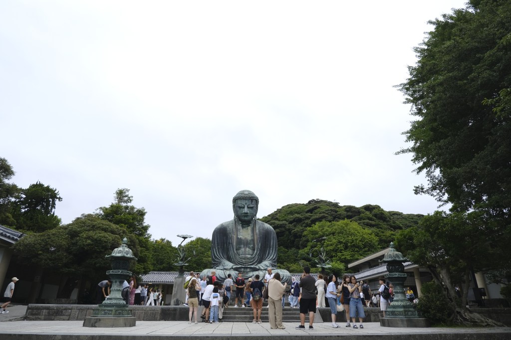 Büyük bir Buddha heykelinin önünde duran turistler.